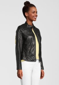 Zwarte leren jack met gewatteerde schouders en getextureerde accenten, voorzien van een staande kraag, ritssluiting aan de voorkant en twee zijzakken.