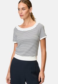 Striped short-sleeve top in white and navy, featuring a wide neckline and ribbed texture, paired with navy trousers.