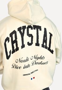 Felpa con cappuccio color crema con audace testo nero: "CRYSTAL", "Nordic Nights" e "Dive into Darkness" con un accento della bandiera francese.