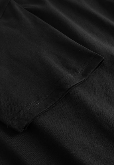 Camiseta de algodão preta com uma textura suave, mangas curtas e decote redondo. Costura neat ao longo da bainha e das bordas das mangas.