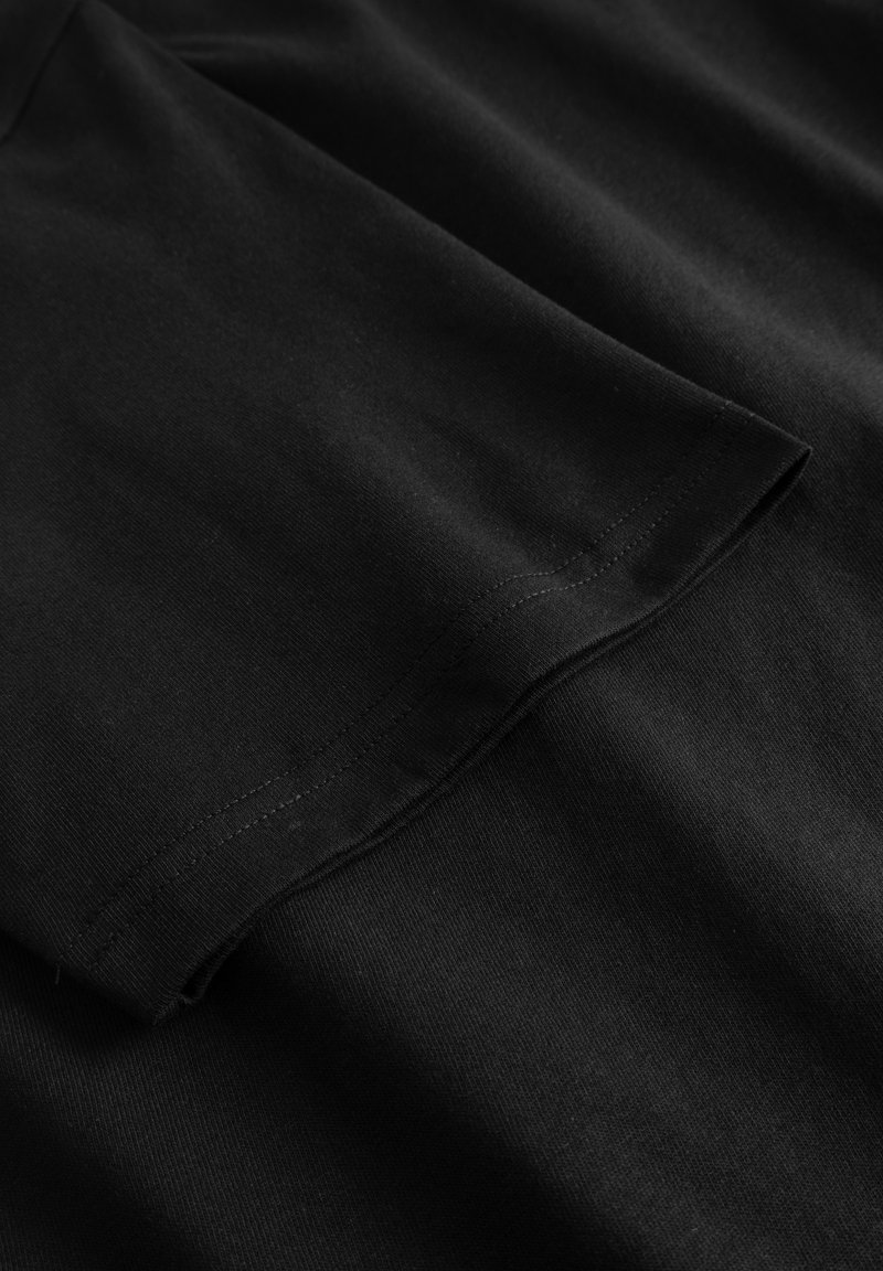 Schwarzes Baumwoll-T-Shirt mit glatter Textur, kurzen Ärmeln und rundem Halsausschnitt. Sorgfältige Nähte entlang des Saums und der Ärmel. 