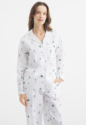 White pajama set featuring a skiing pattern in green, blue, and red. Includes a long-sleeve button-up shirt with pocket and matching pants.