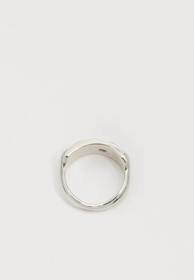 Bague en métal couleur argent avec un design de bande légèrement irrégulier et arrondi sur un fond blanc uni.