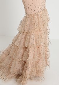 Robe rose pâle à étages avec tissu en tulle superposé orné de petits motifs floraux dorés brillants.