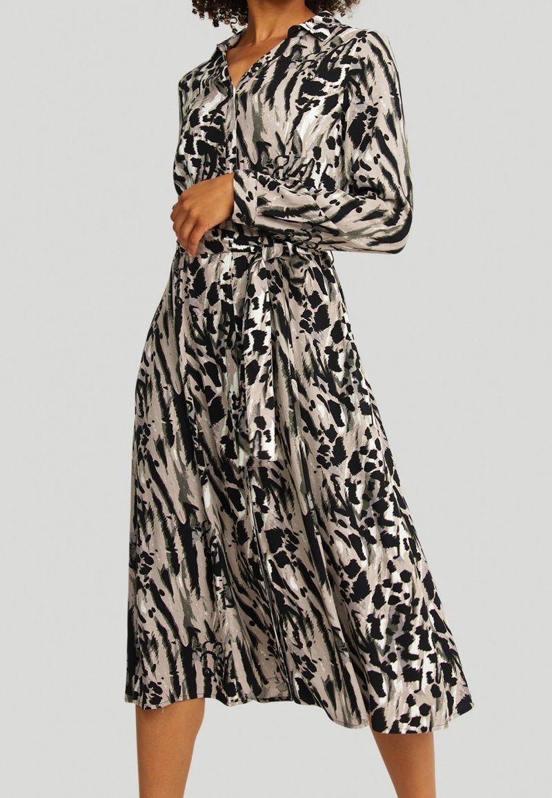 Femme portant une robe à manches longues boutonnée avec un imprimé animal abstrait noir, blanc et gris et une ceinture nouée à la taille.