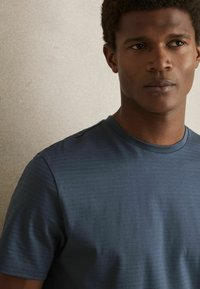Tricou scurt cu maneci, de culoare albastru închis, realizat dintr-un material texturat cu dungi orizontale subtile și guler rotund.