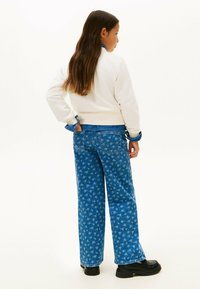 Felpa bianca con polsini e orlo a coste, abbinata a jeans a gamba larga con stampa floreale blu e scarpe nere chunky.