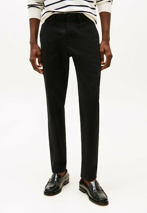 Pantalones negros ajustados con textura suave, bolsillos frontales y cierre de botón, combinados con mocasines negros.