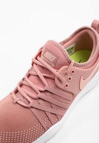 Treningowe buty Nike w delikatnym różowym kolorze, z siateczkową cholewką, dopasowanymi sznurowadłami, plastikowymi akcentami oraz białą podeszwą z teksturowanym wzorem zapewniającym przyczepność.