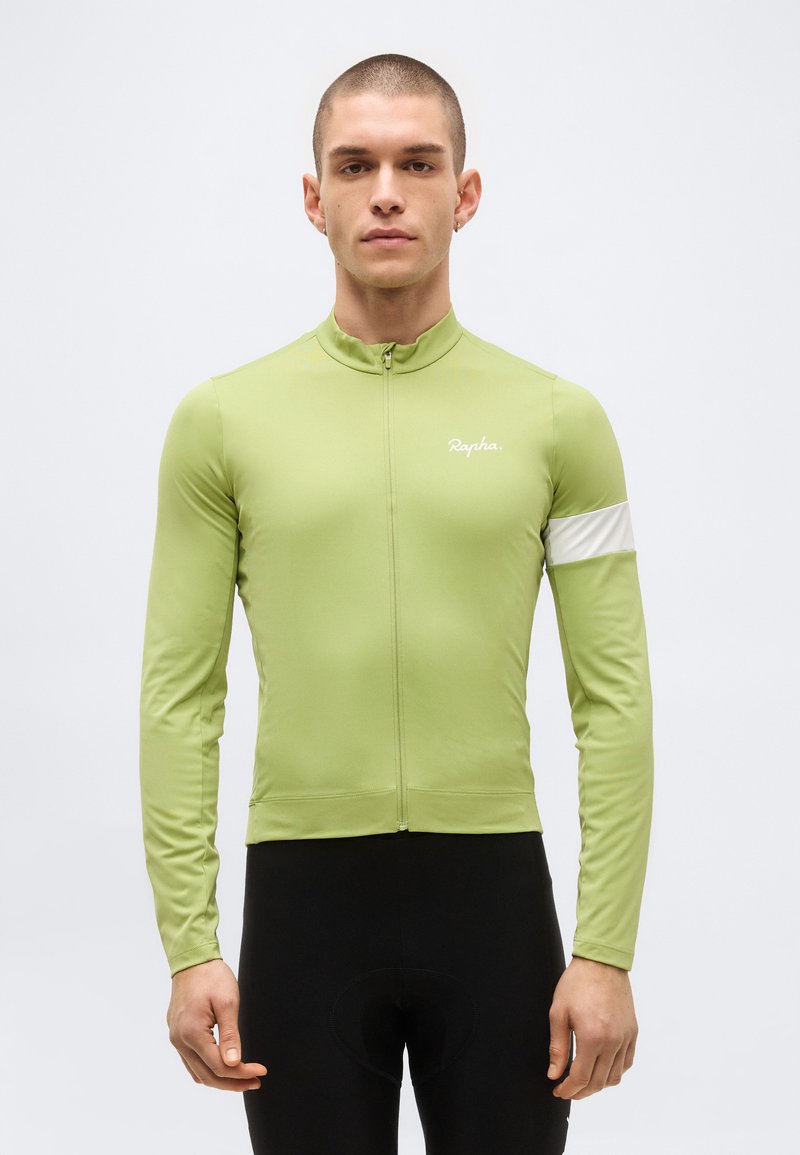 Άνδρας που φοράει ανοιχτό πράσινο μακρυμάνικο ποδηλατικό μπλουζάκι με λευκή ρίγα στον αριστερό βραχίονα και μαύρο ποδηλατικό παντελόνι, όρθιος στραμμένος προς τα εμπρός.