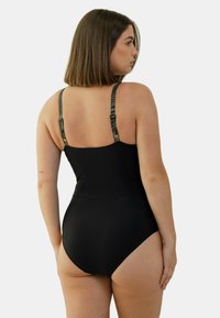 Maillot de bain noir une pièce avec des bretelles à motif contrastant. Texture lisse et design ajusté, avec une taille haute et une couverture modeste à l'arrière.