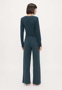 Ensemble de détente côtelé teal comprenant des manches longues, un col rond et un pantalon à jambes larges avec une coupe décontractée. Texture de tissu douce.