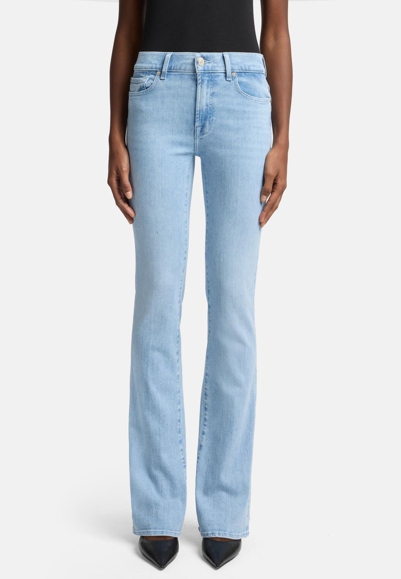 Jeans svasati in denim azzurro chiaro con vita alta, dotati di tasche frontali e chiusura con bottone classico. Indossati con scarpe nere a punta.