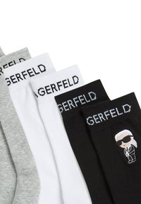 Päť párov ponožiek v sivej, bielej a čiernej bavlne. Každé má logo pásku s nápisom "GERFELD" a na čiernom páre sa nachádza grafika postavy.