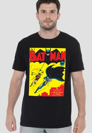 Mann trägt schwarzes T-Shirt mit Vintage Batman-Comic-Cover, auf dem Batman und Robin vor einem hellgelben Hintergrund schwingen.