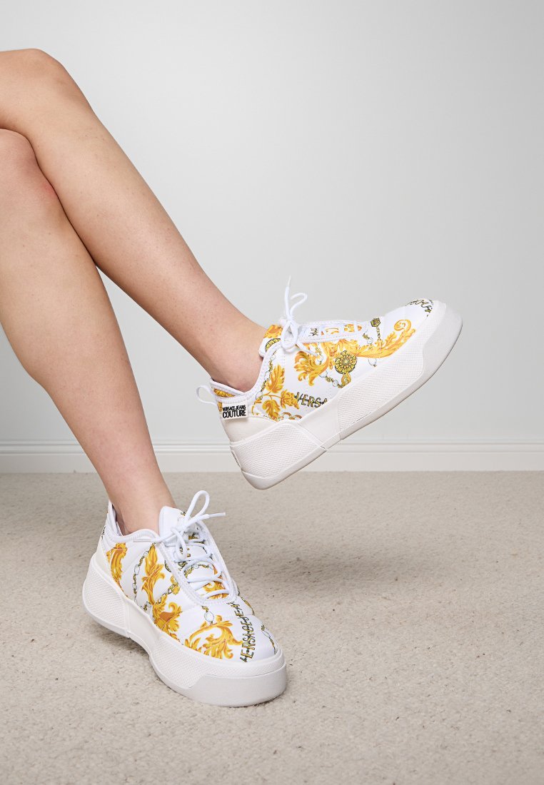 Weiße Sneakers mit bunten Blumen- und geschmackvollen Mustern, strukturierter Sohle und weißen Schnürsenkeln. Mit Branding an der Seite und im Zungenbereich.