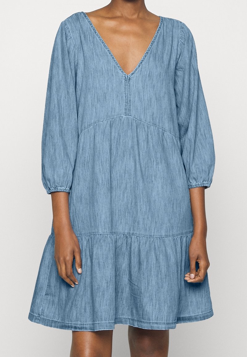 Robe en denim bleu avec col en V, manches trois-quarts et ourlet à étages. Caractérisée par un tissu texturé et des poignets de manches élastiqués.