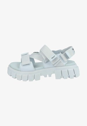 Sandales blanches sportives avec des sangles grises ajustables, une semelle intérieure texturée et une semelle en caoutchouc blanc épaisse dotée de profondes rainures pour une meilleure adhérence.