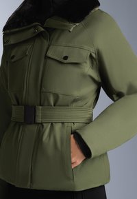 Olivnozelen puffer jakna z pasom v pasu, velikimi žepi na prsih in umetnim krznom okoli ovratnika. Gladka tekstura z detajli na rokavih.
