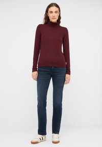 Bordo tekstūruotas su apykakle megztinis su ilgomis rankovėmis, derinamas su vidutinio plovimo džinsais ir kreminiais sportbačiais su juodais akcentais.