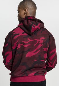 Felpa con cappuccio a motivo camouflage color maroon e rosa, dotata di cordino, polsini e orlo a coste, realizzata in tessuto morbido, che presenta un design urbano.