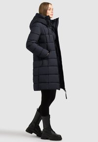 Námorní pufák s kapucí, prošívaný design, boční kapsy a celopřístupný zip. Kombinováno s černými legínami a robustními černými botami.