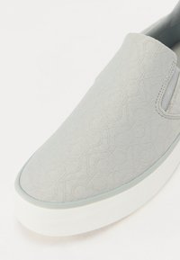 Lihtsa halli tekstuuriga kanga ülaservaga slip-on jalanõud, millel on geomeetriline muster ja valge kummist tald. Minimalistlik disain, millel on elastsed külgpaneelid.