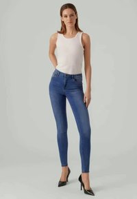 Peenikesed sinised teksad, mis on valmistatud denimist, kõrge vöökoht, puhas disain ja sile tekstuur. Kantud sobiva valge topi ja kontsadega.