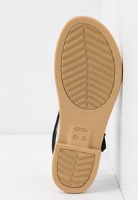 Semelle de sandale en caoutchouc beige avec motif de bande de roulement en chevrons, taille marquée W 5, nom de la marque "crocs" embossé au bas.