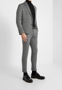 Grå mönstrad kostym med slim fit, knäppt kavaj och matchande byxor, kombinerat med en svart rullkrage och svarta finskor.