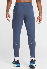 Navy blue athletic pants with a fitted design, featuring reflective accents and zippers at the ankles. Made from lightweight, moisture-wicking material.