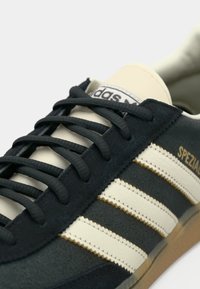 Ανδρικά αθλητικά παπούτσια Adidas με μπλε σκουρόχρωμο σουέντ πάνω μέρος, κρεμ δερμάτινες ρίγες, μαύρα κορδόνια και ελαστική σόλα σε ανοιχτό καφέ χρώμα. Με λεπτομέρεια "SPEZIAL".