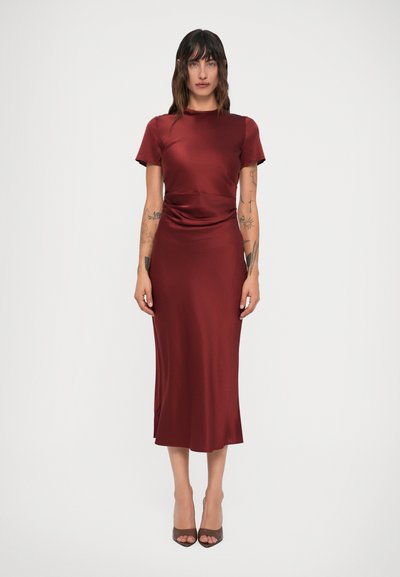 Robe satin bordeaux à manches courtes et à taille ajustée, dotée d'une fente sur le côté et d'une texture lisse. Accessoirisée avec des chaussures à talons ouverts.