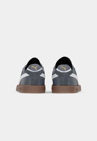 Szare sneakersy z teksturowanym zamszowym obcasem, białymi paskami po bokach i brązowymi gumowymi podeszwami. Zawierają złote logo na pięcie i języku.