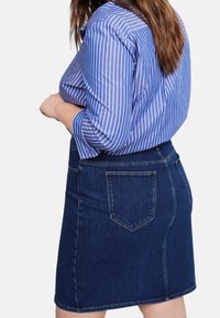Falda de mezclilla en azul oscuro con una silueta recta, que cuenta con bolsillos traseros y una textura suave, combinada con una camisa a rayas azul y blanca.