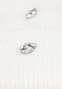 Tessuto a costine crema con tre decorazioni in strass trasparenti, di diverse dimensioni e forme, posizionate sulla superficie.