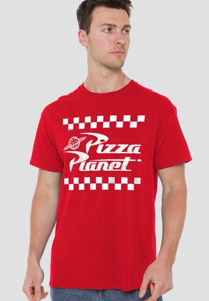 Mann trägt rotes T-Shirt mit weißem "Pizza Planet"-Schriftzug und kariertem Design, schaut seitlich vor einfarbigem Hintergrund.