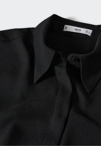 Black, collared blouse made of smooth fabric, featuring a button closure and subtle stitching details. Simple, minimalist design.