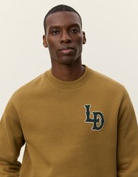 Sweatshirt vert olive avec un col rond, des poignets côtelés et un logo brodé texturé en vert et blanc sur la poitrine.