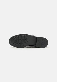 Suela de zapato negra con una superficie texturizada. Presenta un patrón de surcos profundos y un borde redondeado para un mayor agarre y estabilidad.
