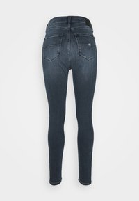 Dark indigo skinny jeans with a smooth texture, featuring a high waist, two back pockets, and a branded waistband accent.