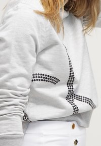 Sudadera gris con patrón de puntos negros, con un corte relajado y mangas largas. La tela parece suave y tiene puños de canalé.