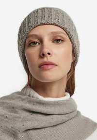 Szara dzianinowa czapka z prążkowaną fakturą i srebrnymi zdobieniami, zestawiona z jasnoszarym swetrem ozdobionym rozproszonymi srebrnymi koralikami.