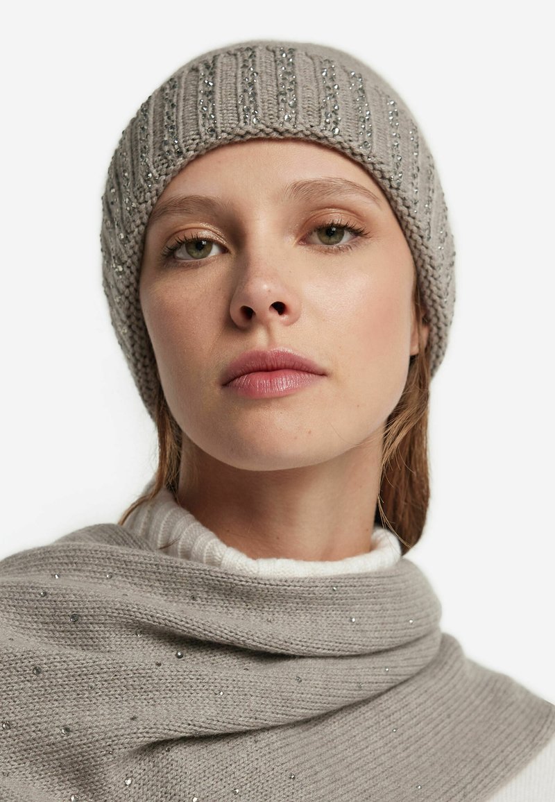 Szara dzianinowa czapka z prążkowaną fakturą i srebrnymi zdobieniami, zestawiona z jasnoszarym swetrem ozdobionym rozproszonymi srebrnymi koralikami.