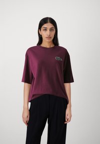 T-shirt in cotone bordeaux con maniche corte e scollatura rotonda. Presenta un piccolo logo ricamato verde sul petto.