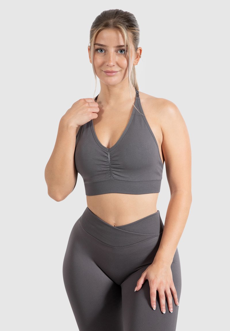 Grijze sportbeha met een geplooid voorkantdetail en halterbandjes, gecombineerd met hoge grijze leggings. Gladde, rekbare stof.