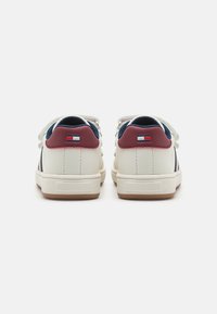 White leather sneakers with navy accents and burgundy heel tabs. Features textured rubber soles and flat white laces. Small logo on the heel.