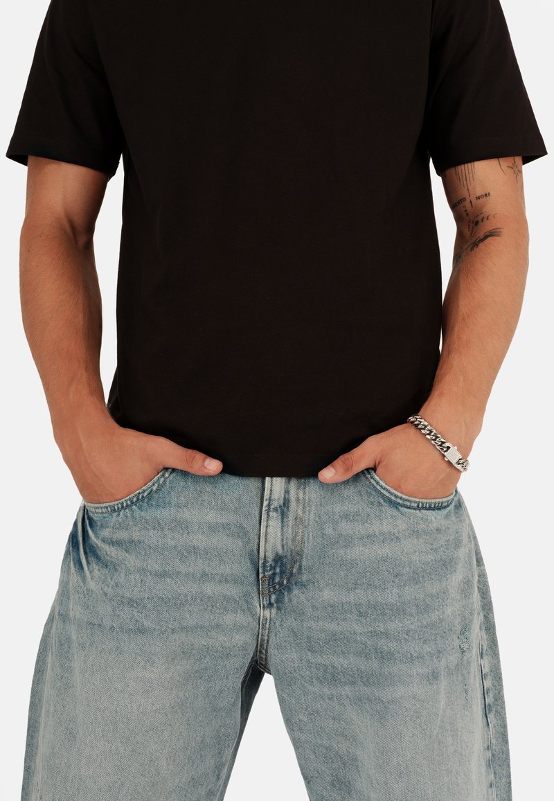 Schwarzes Baumwoll-T-Shirt kombiniert mit hellblauen, abgetragenen Jeans. Schlichtes Design mit kurzen Ärmeln und lockerer Passform. Silbernes Armband sichtbar.
