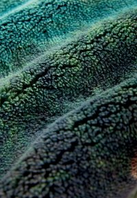 Textúrovaná fleece tkanina v rôznych odtieňoch zelenej s mäkkým, nadýchaným povrchom a krčeným vzhľadom, ktorý ukazuje hĺbku a dimenziu.