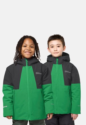 Zwei Kinder tragen grüne und dunkelgraue Jack Wolfskin-Jacken mit Kapuze, stehen nebeneinander und schauen mit Blick zur Kamera vor einem schlichten Hintergrund.